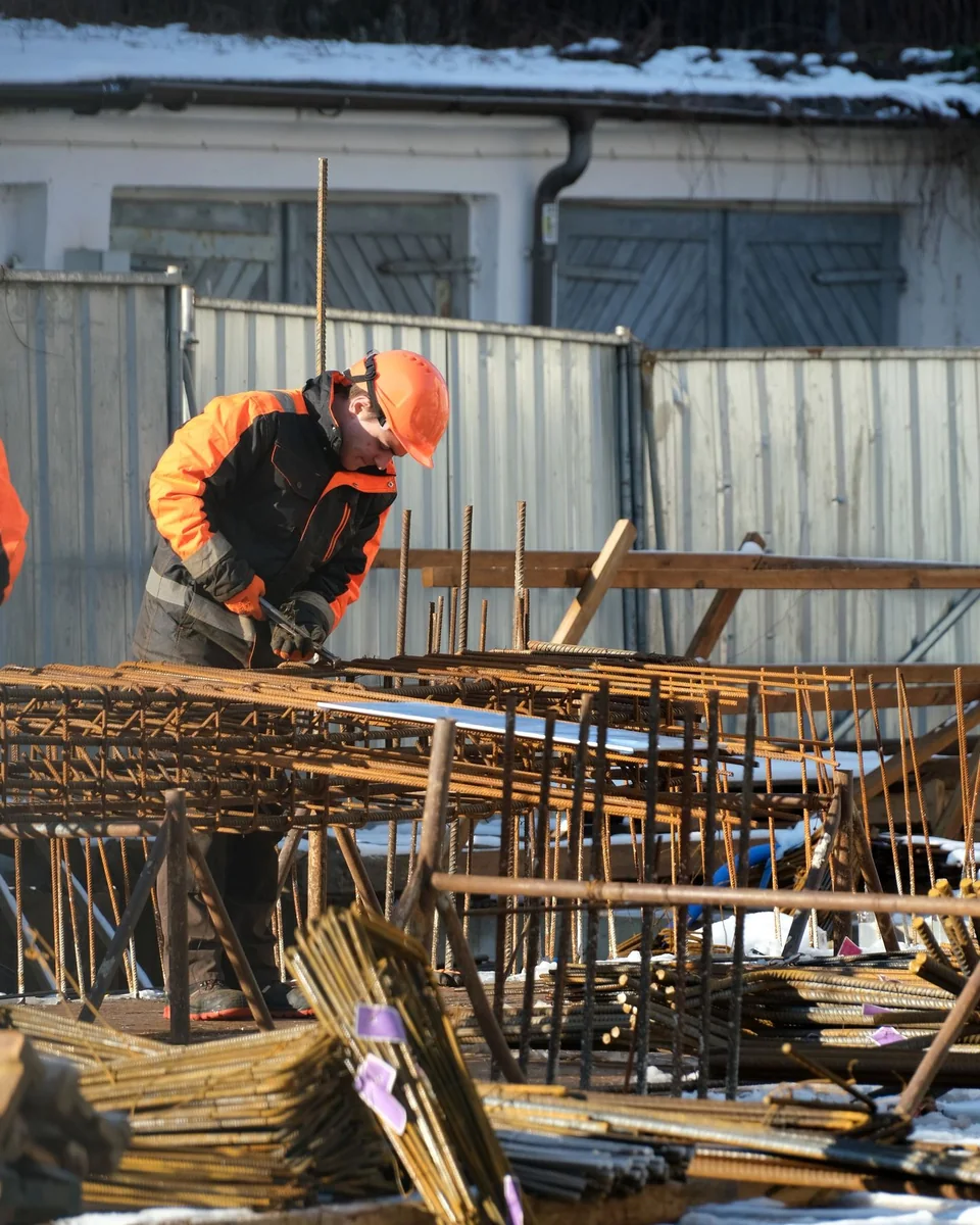 Ouvrier en casque orange assemblant des armatures sur un chantier.