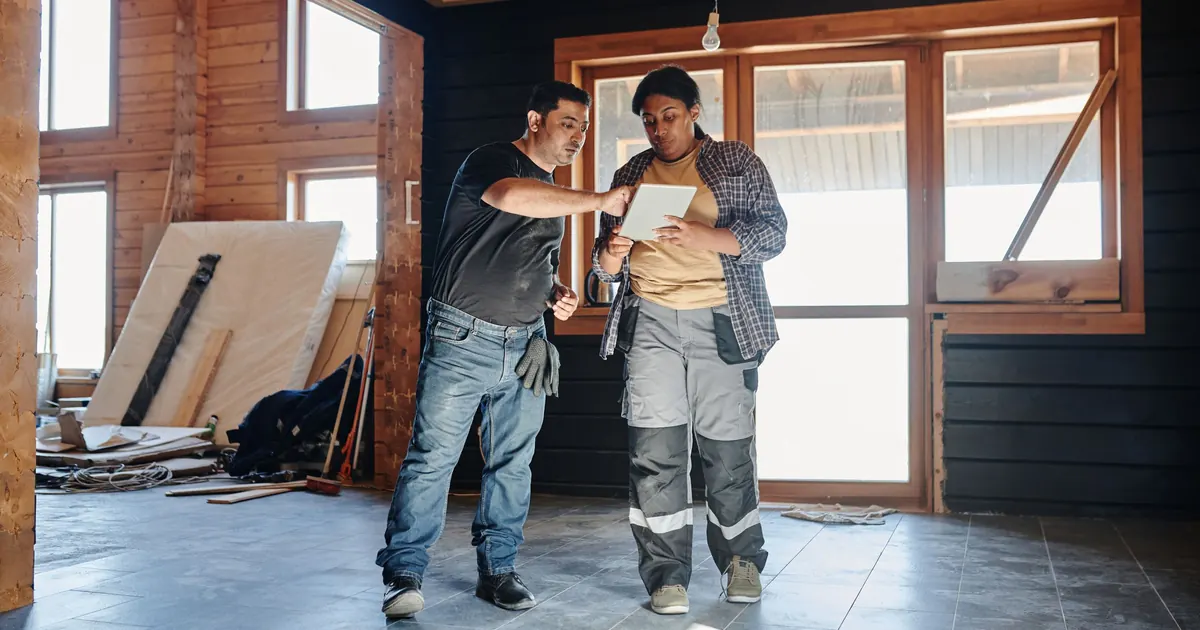 Deux professionnels du bâtiment consultent une tablette dans un chantier de rénovation.