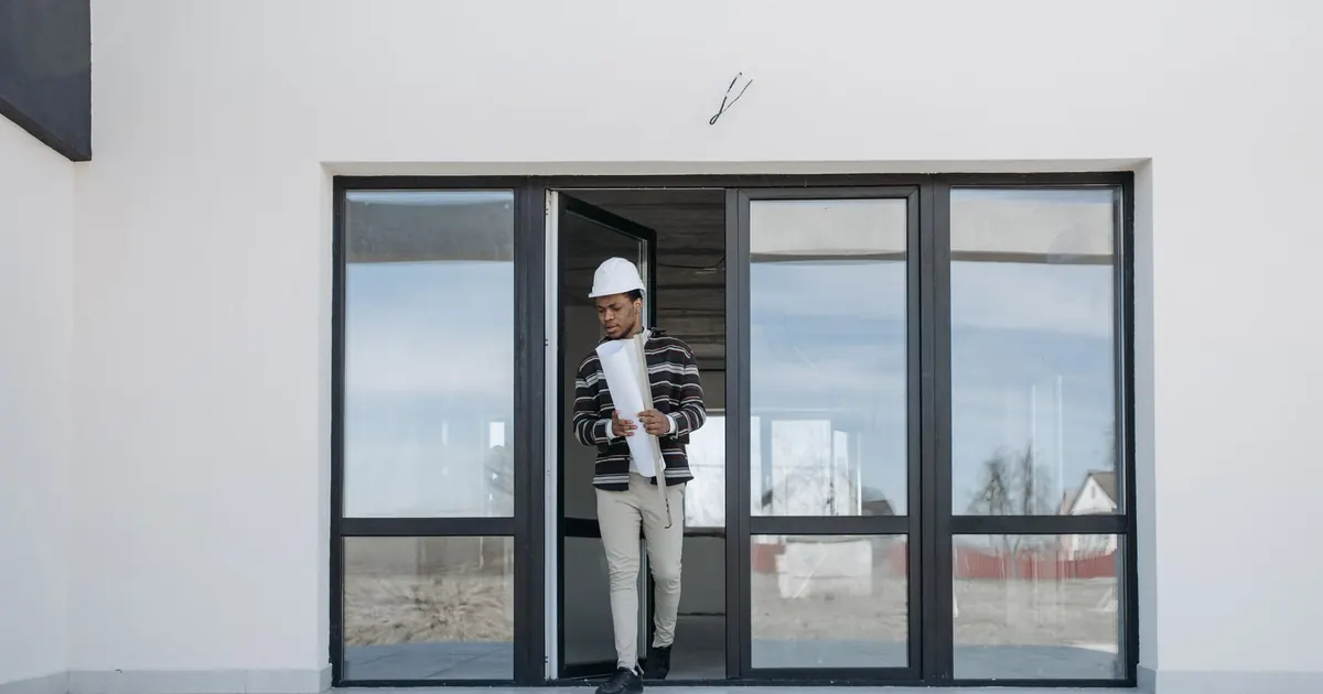 Personne équipée d’un casque tenant des plans devant un bâtiment