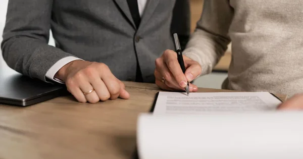 Deux personnes examinent un document posé sur une table, stylo en main.