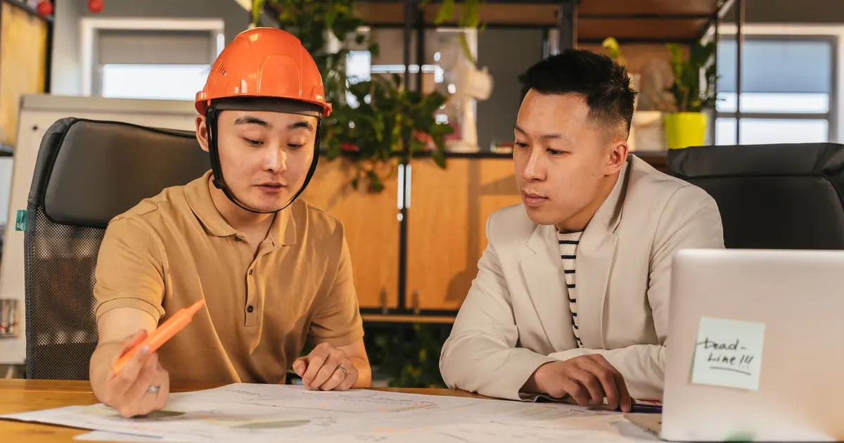 Deux professionnels du bâtiment relisent des documents et des plans dans un bureau.
