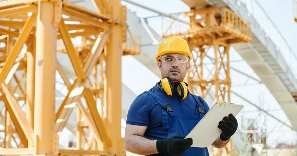 Professionnel équipé d’un casque vérifiant un chantier avec un support de notes.