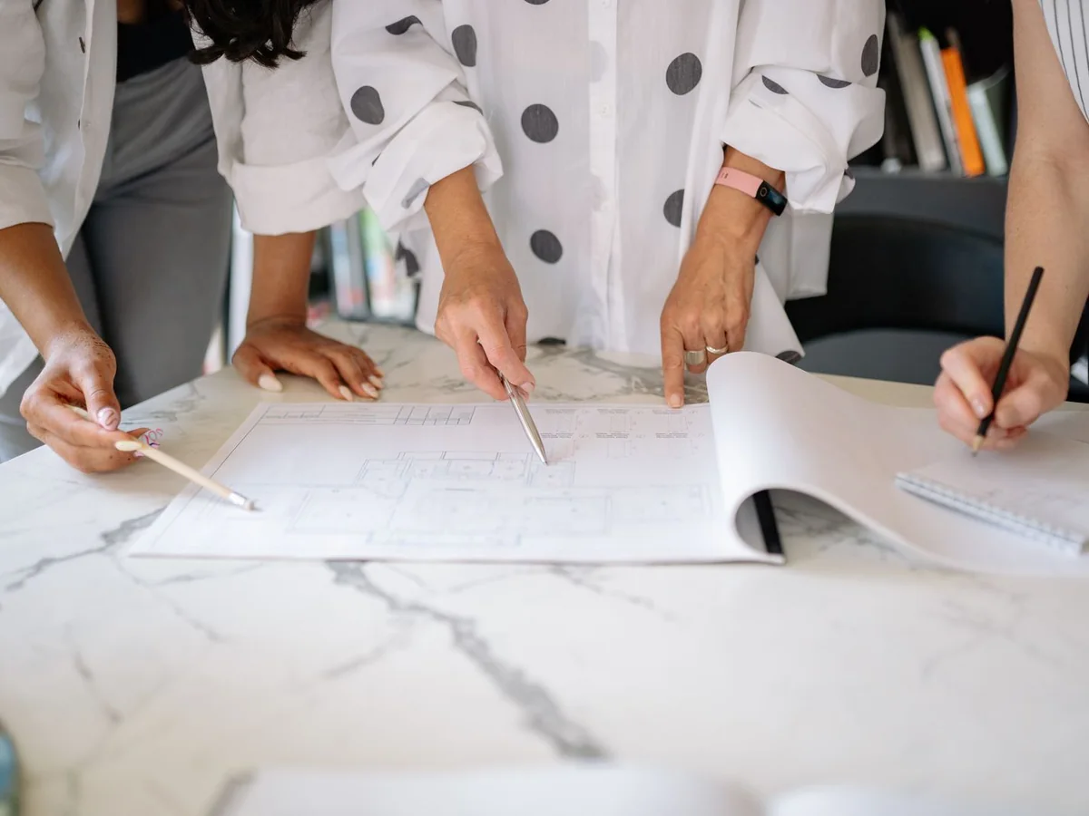 Plusieurs personnes examinent et annotent un plan de bâtiment sur une table.